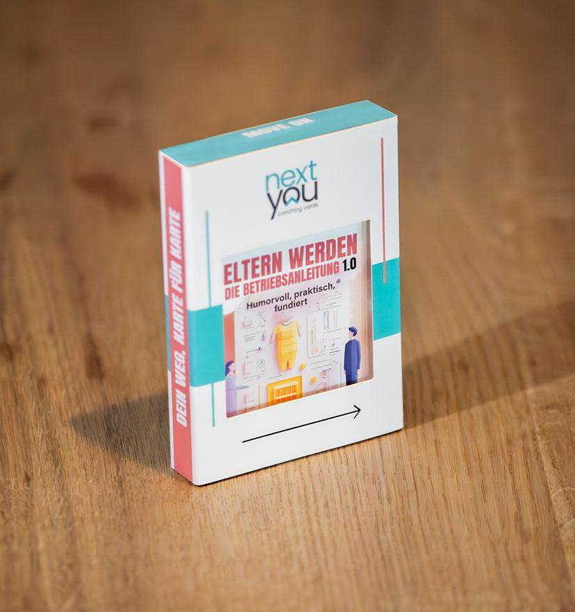 Das NextYou Kartenset „Eltern werden – Die Betriebsanleitung 1.0“ liegt auf einem Tisch – bereit zum Auspacken. Die stilvolle Verpackung macht Lust aufs Entdecken: humorvolle, fundierte und alltagsnahe Inhalte für werdende Eltern. Ideal für alle, die sich mit einem Augenzwinkern auf das Abenteuer Familie vorbereiten wollen.