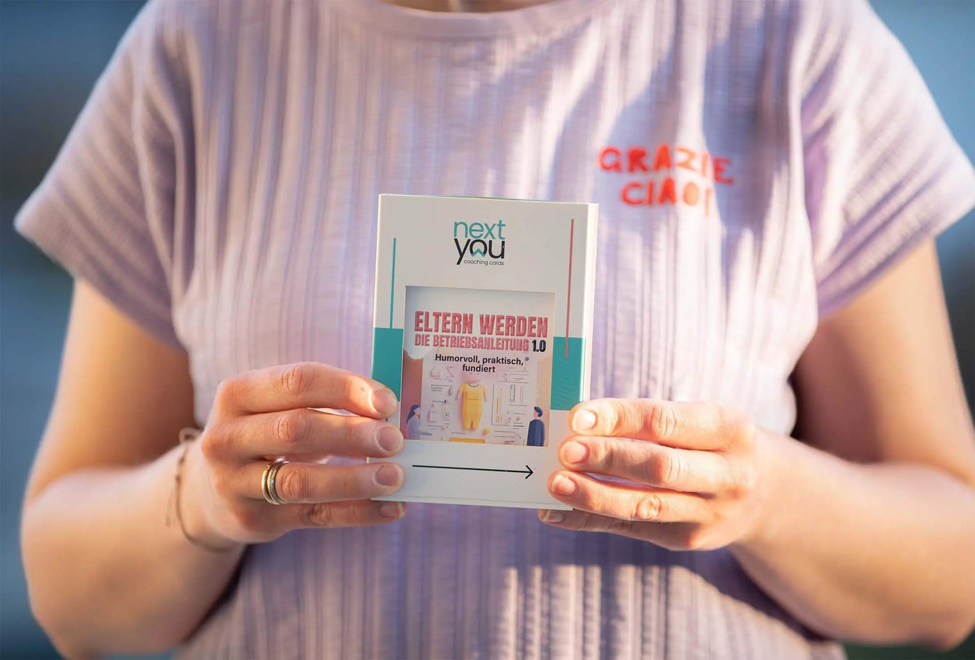 Das Coaching-Kartenset „Eltern werden – Die Betriebsanleitung 1.0“ von NextYou wird von einer Frau im Sonnenlicht in die Kamera gehalten. Die Subline „humorvoll, praktisch, fundiert“ spiegelt den Charakter des Sets wider – ein liebevoll gestalteter Wegbegleiter für werdende Eltern. Mit echten Tipps, alltagsnahen Aufgaben und einer Prise Humor vermittelt dieses Set fundiertes Wissen rund um Schwangerschaft, Geburt und die ersten Baby-Monate.