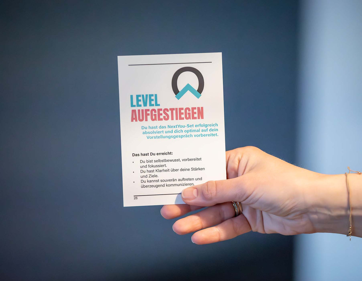 Ein symbolischer Abschluss: Eine Hand hält die letzte Karte aus einem NextYou Coaching Card Set hoch – mit der motivierenden Botschaft „Level aufgestiegen!“. Diese Abschlusskarte fasst die erreichten Ziele zusammen und zeigt, worin man sich persönlich verbessert hat. Ein echter Meilenstein für alle, die sich mit dem Set weiterentwickelt haben – egal ob im Beruf, Alltag oder kreativen Projekten. Perfekt als Motivation und zur Reflexion des eigenen Fortschritts.